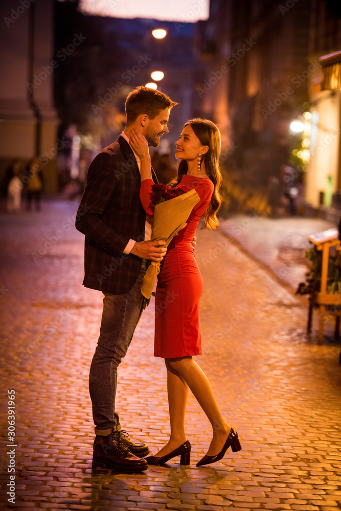 happy, elegant girl hugging boyfriend holding bouquet of red roses on night street