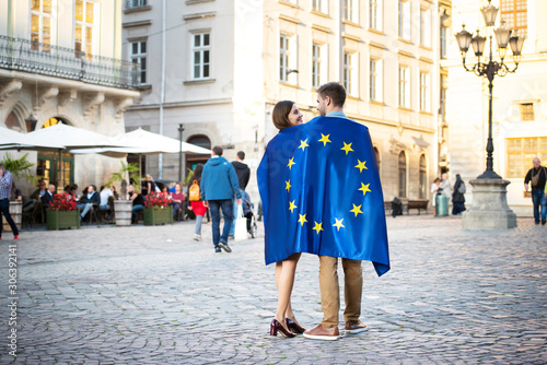 couple of young tourists, wrapped in flag of european union, standing on city square