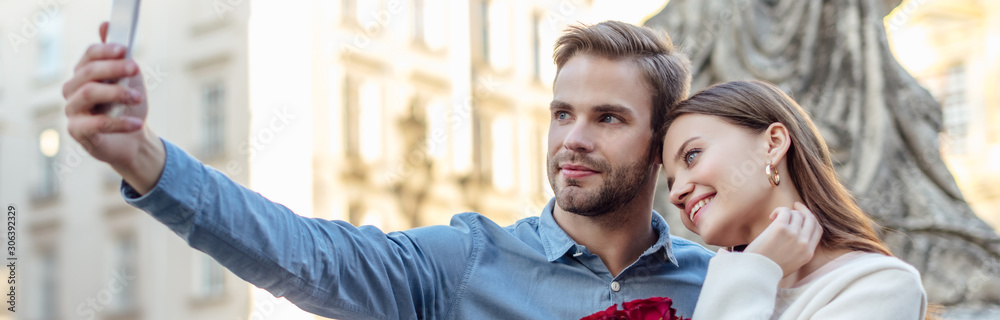 panoramic shot of handsome man taking selfie on smartphone with happy girlfriend panoramic shot of handsome man taking selfie on smartphone with happy girlfriend
