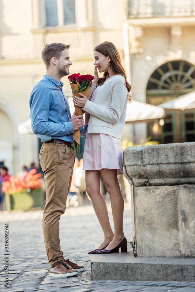 handsome man presenting bouquet of roses to happy girlfriend on street