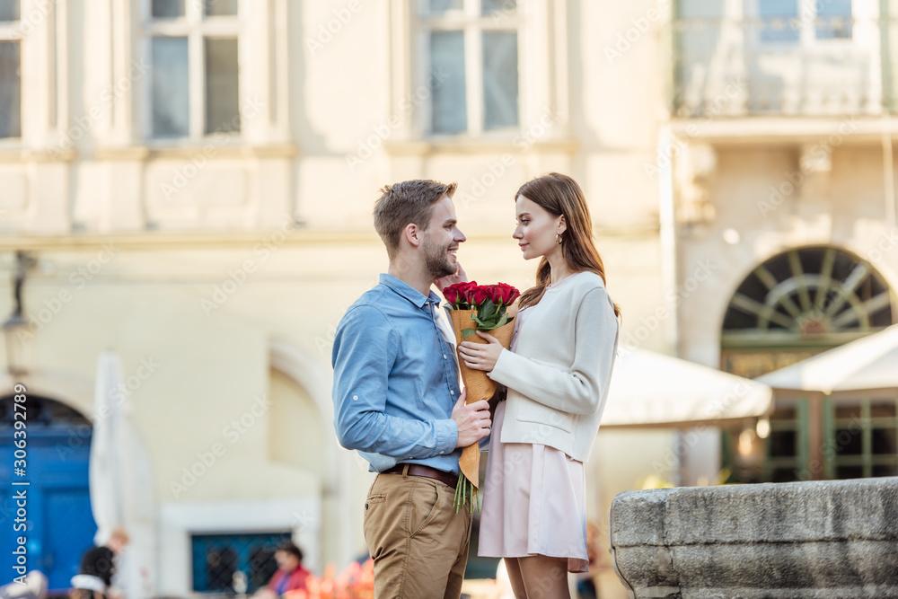 handsome man presenting bouquet of roses to happy girlfriend on street handsome man presenting bouquet of roses to happy girlfriend on street