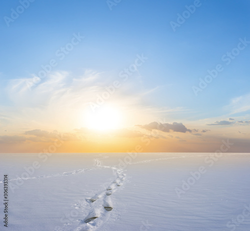 winter snowbound plain with human track at the sunset