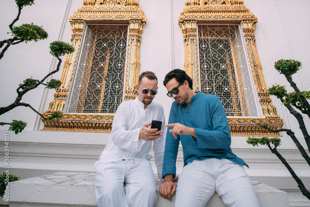 Men in a Buddhist temple read tourist information, look at a map on the phone.