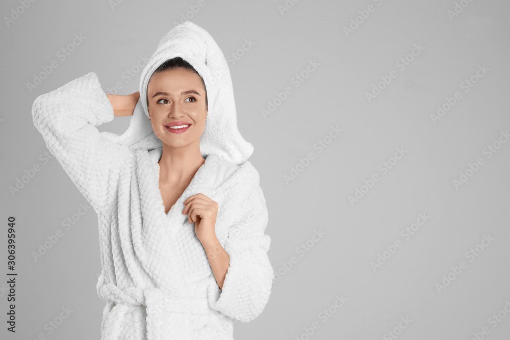 Obraz premium Beautiful young woman in bathrobe on light grey background. Space for text