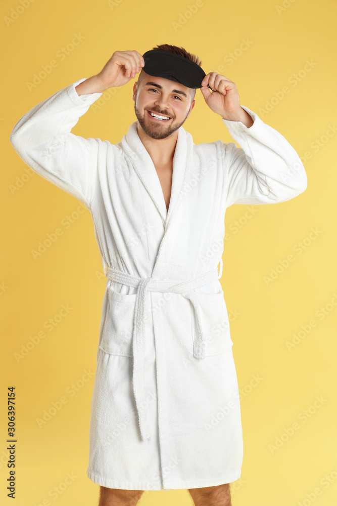 Young man in bathrobe and eye sleeping mask on yellow background