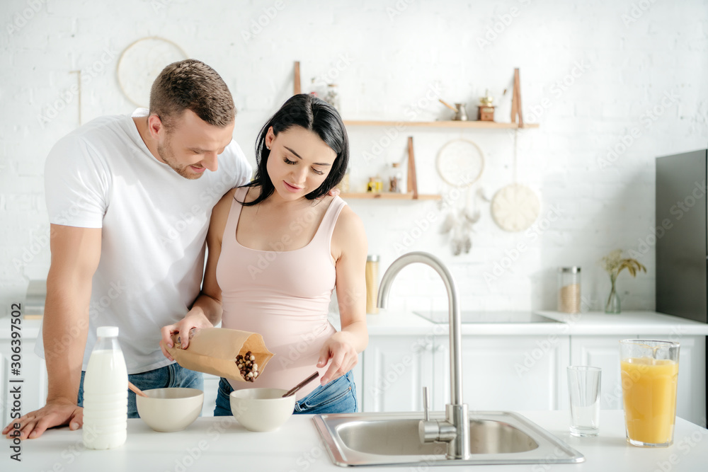 happy pregnant couple with cereals, milk and orange juice in kitchen happy pregnant couple with cereals, milk and orange juice in kitchen