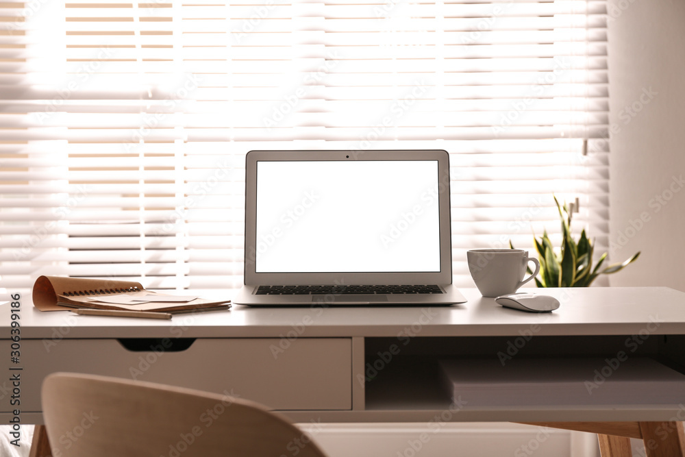 Fototapeta premium Laptop on desk near window in office. Comfortable workplace
