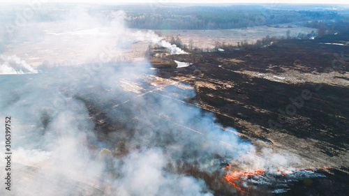 Forest and field fire. Dry grass burns, natural disaster. Aerial view. Smooth flight over the place of fire, a small stream blocks the path to the fire.