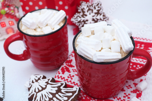 two red mugs of coffee and marshmallows, gingerbread with icing in the form of a Christmas tree snowflakes, cupcakes in the form of houses on a red and white towel, a red gift box, toy house..