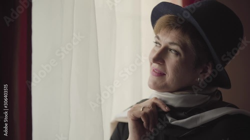 Close-up face of thoughtful Caucasian woman in stylish hat and scarf looking out the window. Portrait of beautiful confident retiree thinking. photo