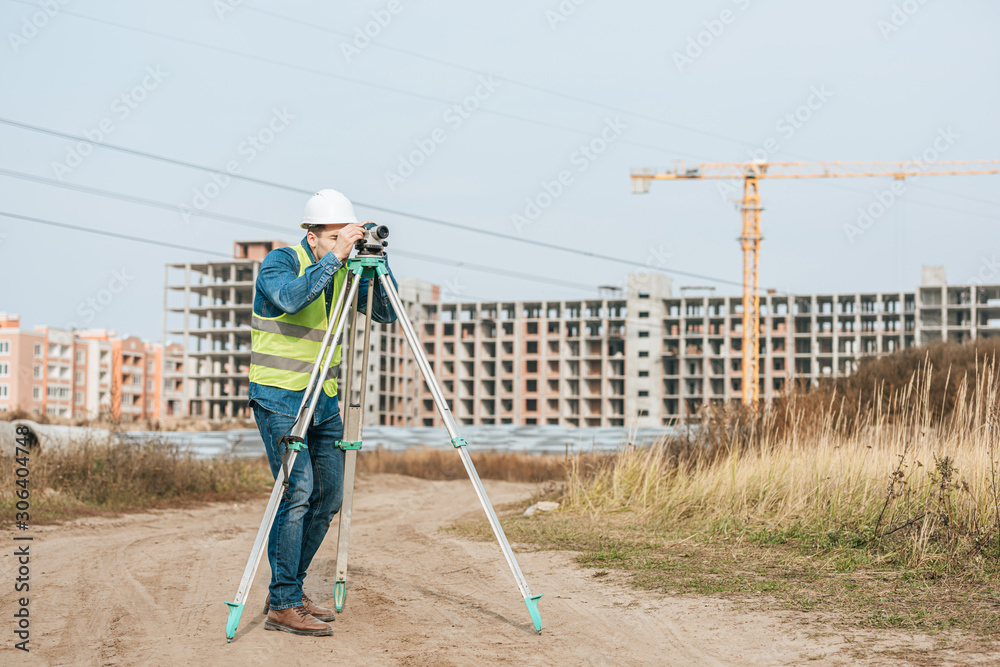 Surveyor looking through digital level on dirt road of construction site