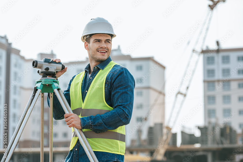 Smiling surveyor with digital level looking away on construction site Smiling surveyor with digital level looking away on construction site