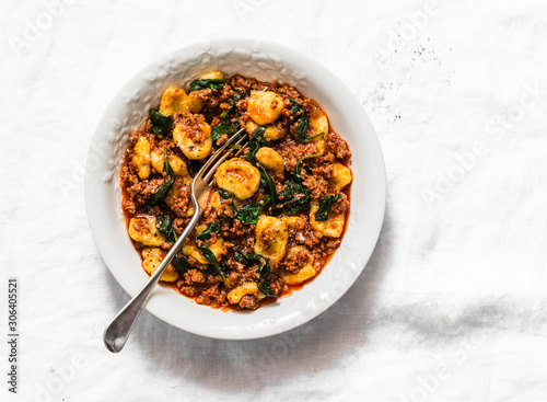 Pumpkin gnocchi with bolognese sauce and spinach on a light background, top view