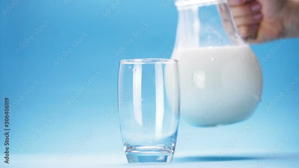 milk is poured into a glass on blue background milk is poured into a glass on blue background