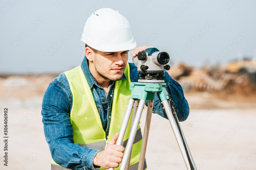 Surveyor in hardhat and high visibility jacket looking in digital level Surveyor in hardhat and high visibility jacket looking in digital level