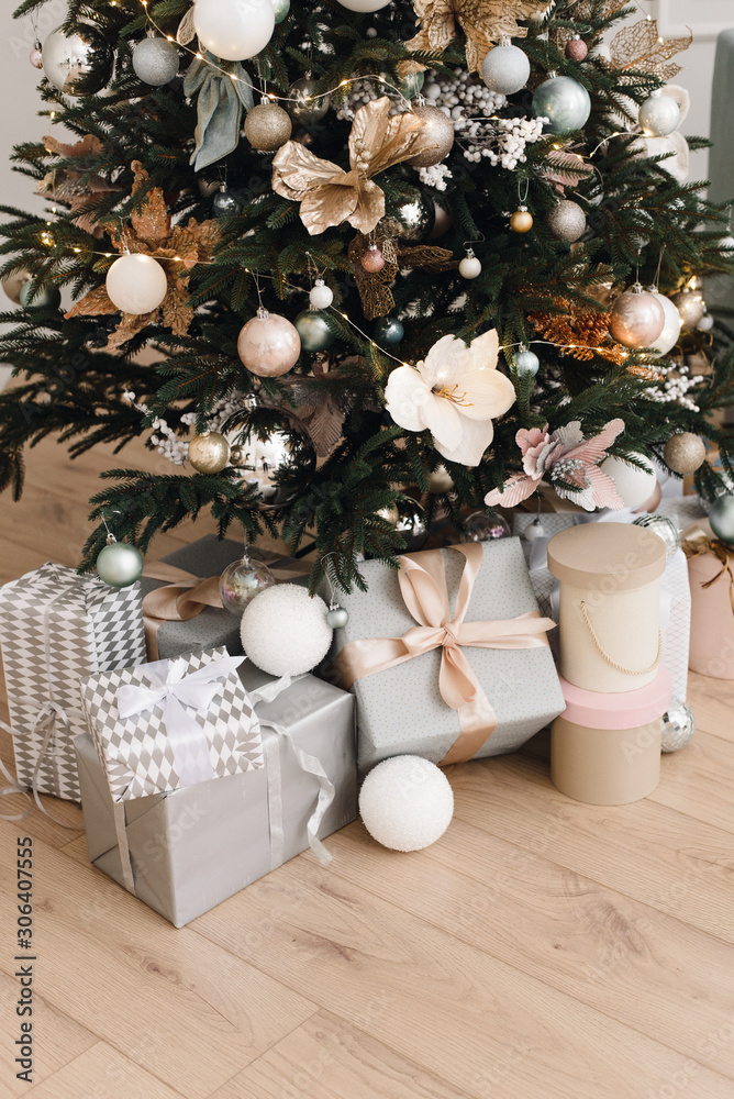 Bright silver gifts in packaging and with bows under the Christmas tree on the floor. Christmas decorations. Christmas background. Beautiful holiday decorated room Bright silver gifts in packaging and with bows under the Christmas tree on the floor. Christmas decorations. Christmas background. Beautiful holiday decorated room