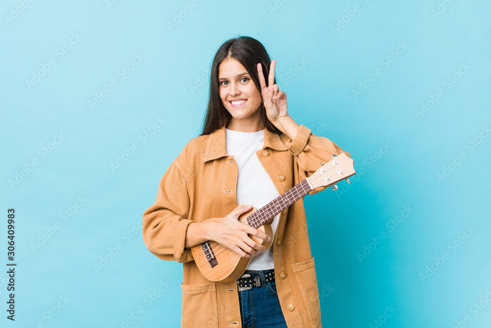 Young caucasian woman holding a ukelele showing victory sign and smiling broadly. Young caucasian woman holding a ukelele showing victory sign and smiling broadly.