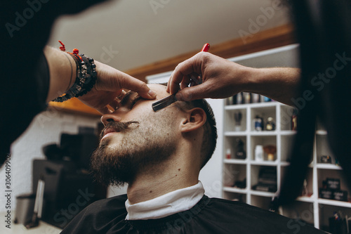 stylish attractive man with a beard in a barbershop. Shaving and modeling a contemporary beard shape in retro style, the barber shaves his client