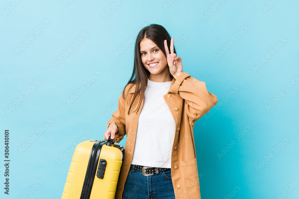 Young caucasian woman holding a suitcase showing victory sign and smiling broadly. Young caucasian woman holding a suitcase showing victory sign and smiling broadly.