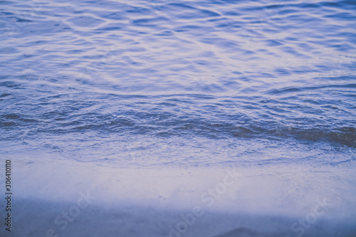 A small wave beats on the shore of the river, lake, sea. Blue shade of water. Close-up of the wave. Calm water. Background.