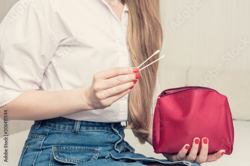 Woman with cotton swabs and cosmetic bag, woman sitting on the bed, woman's hands, cropped image, close up, toned