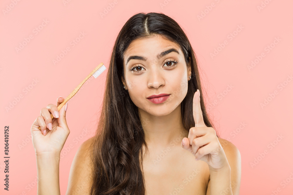Young indian woman holding a toothbrush showing number one with finger. Young indian woman holding a toothbrush showing number one with finger.