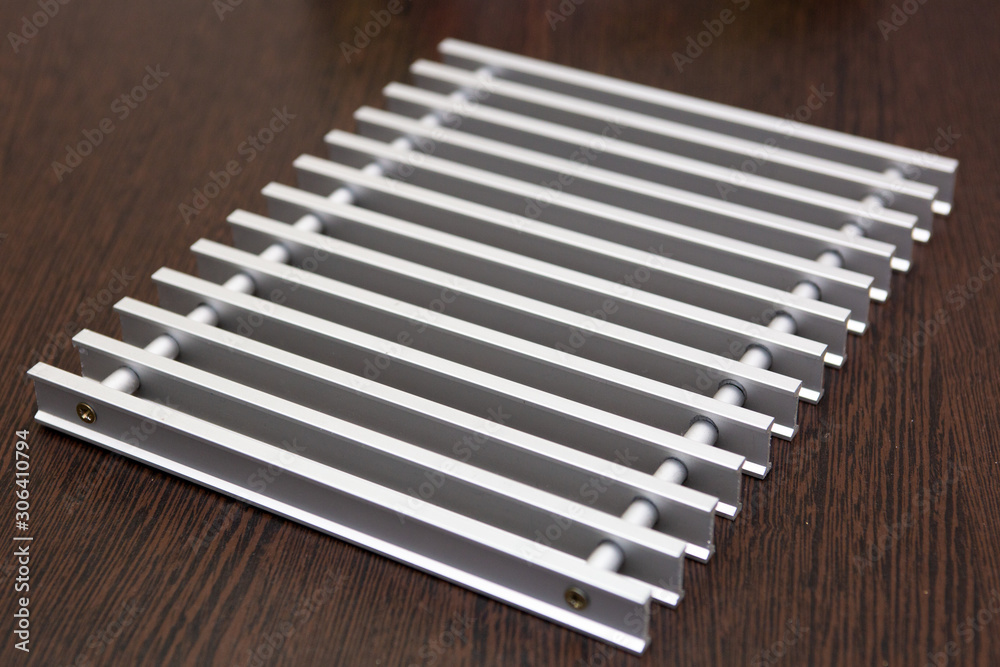 On a dark table lies a lattice of silver metal strips connected by inserts. On a dark table lies a lattice of silver metal strips connected by inserts.