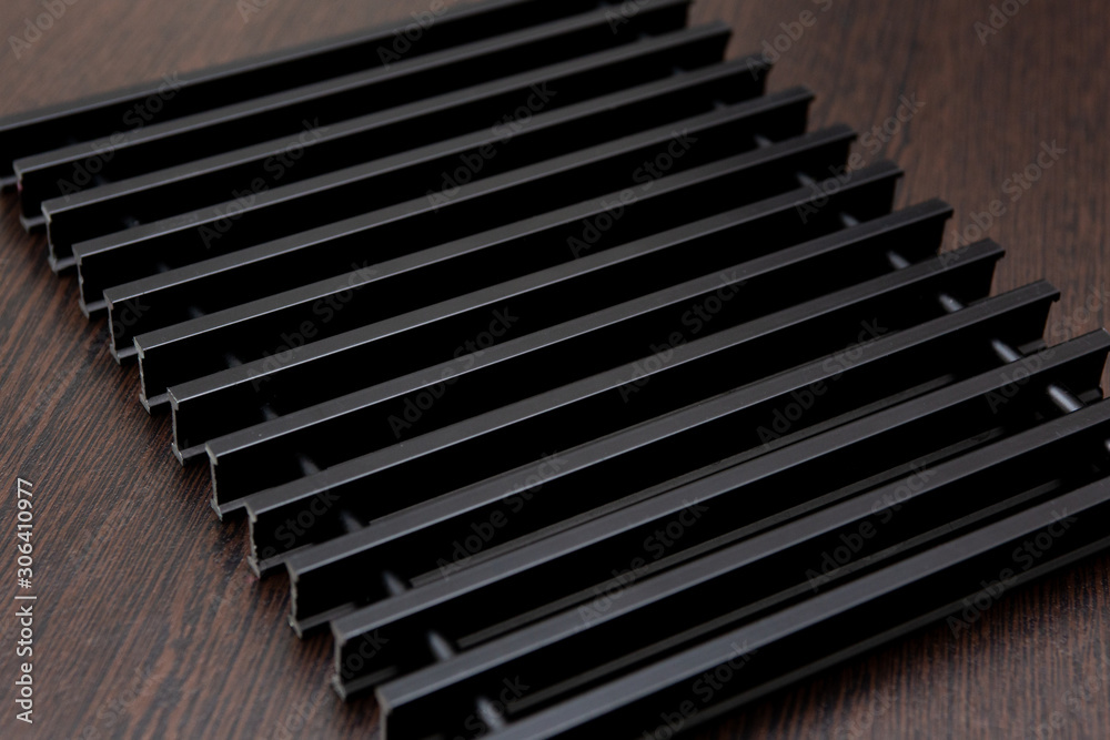 On a dark table lies a lattice of black metal strips connected by inserts. On a dark table lies a lattice of black metal strips connected by inserts.