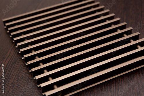 On a dark table lies a grate of chocolate-burgundy metal planks connected by inserts.