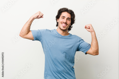 Young handsome man against a white background showing strength gesture with arms, symbol of feminine power