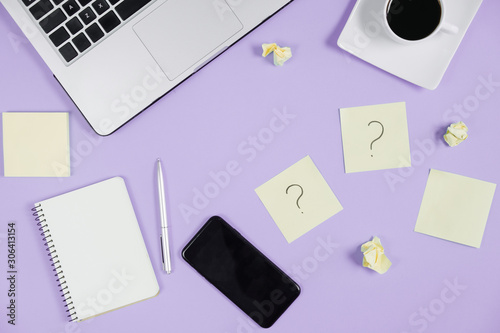 Question mark on sticky notes, notebook, laptop, cup coffee, phone, pen on violet background. FAQ concept. Working with clients. Troubles in work. Flat lay, top view, copy space photo