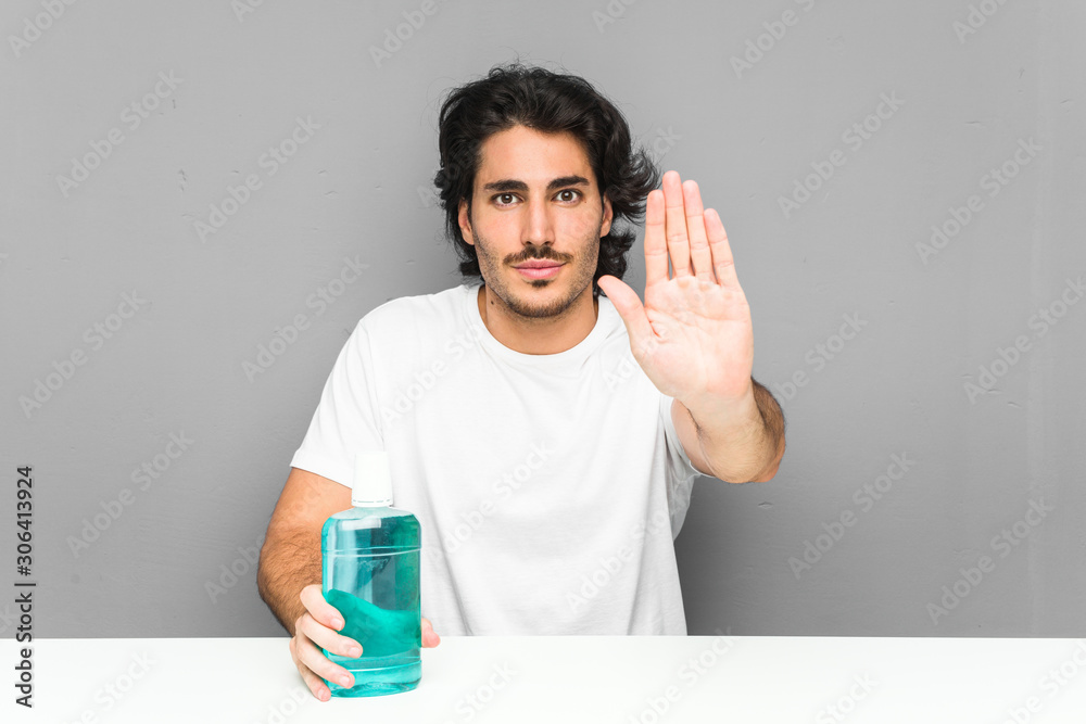 Young man holding a mouthwash standing with outstretched hand showing stop sign, preventing you. Young man holding a mouthwash standing with outstretched hand showing stop sign, preventing you.