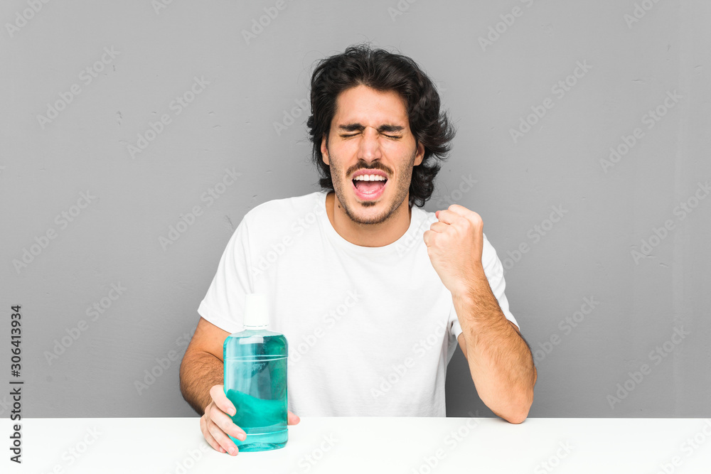 Young man holding a mouthwash cheering carefree and excited. Victory concept. Young man holding a mouthwash cheering carefree and excited. Victory concept.
