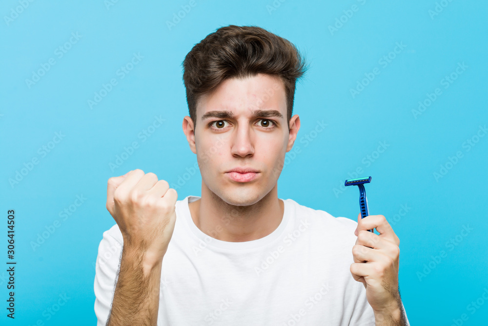 Young caucasian man holding a razor blade showing fist to camera, aggressive facial expression. Young caucasian man holding a razor blade showing fist to camera, aggressive facial expression.