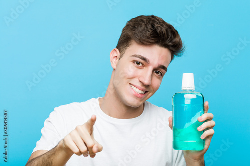 Young caucasian man holding a mouthwash cheerful smiles pointing to front.