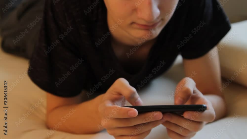 Close-up portrait of young teenager boy texting messages and playng a game using his phone Close-up portrait of young teenager boy texting messages and playng a game using his phone