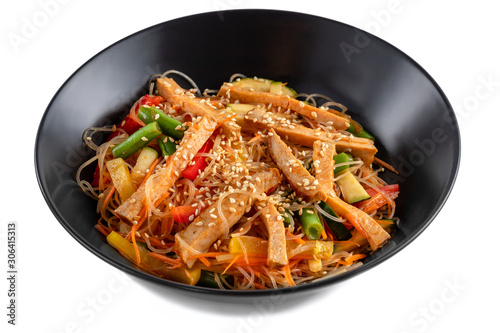 Sliced grilled pork, noodles in sauce, vegetables and sesame seeds in a black plate isolated on white background, side view