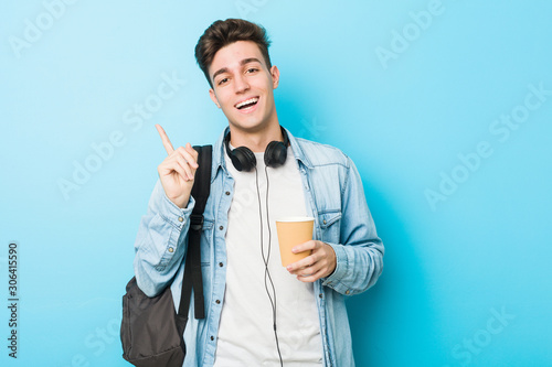 Young caucasian student man holding a take away coffee smiling cheerfully pointing with forefinger away.