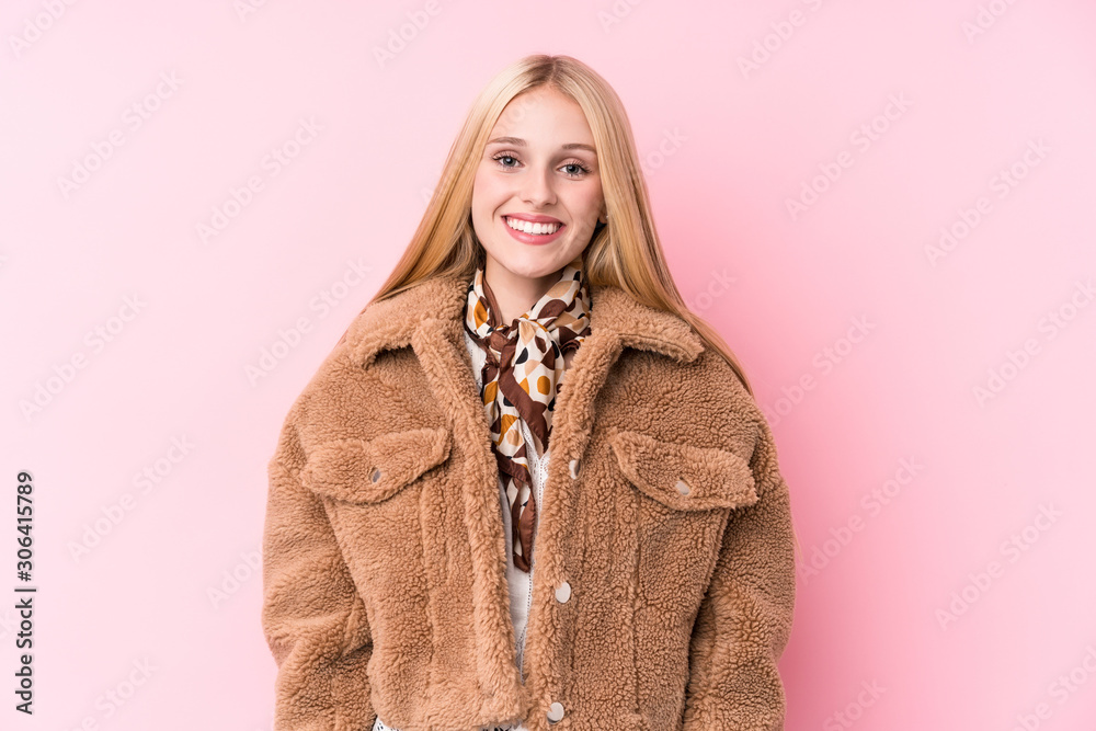 Young blonde woman wearing a coat against a pink background happy, smiling and cheerful. Young blonde woman wearing a coat against a pink background happy, smiling and cheerful.