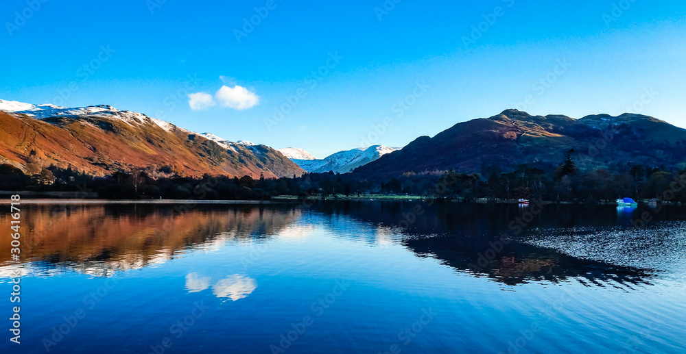 Ullswater, Lake District with mountain reflections in the lake on a calm day with still waters. Snow capped mountains surrounding the second largest lake in the Cumbria, UK.