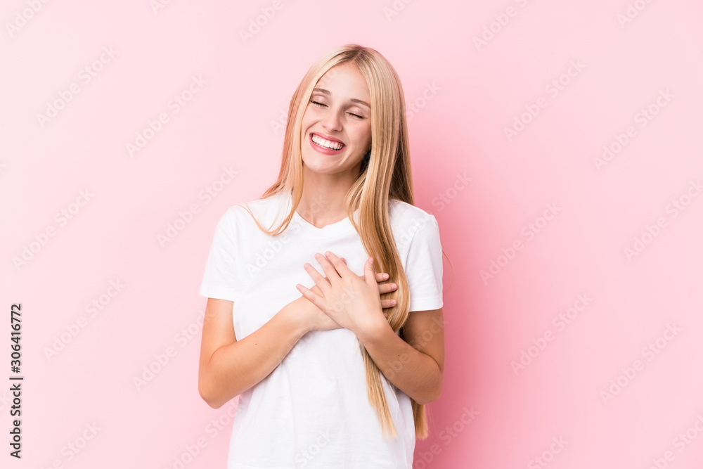 Young blonde woman on pink background laughing keeping hands on heart, concept of happiness. Young blonde woman on pink background laughing keeping hands on heart, concept of happiness.