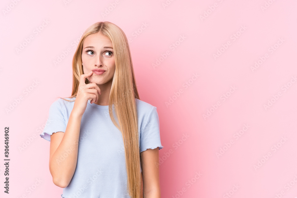 Young blonde woman on pink background looking sideways with doubtful and skeptical expression. Young blonde woman on pink background looking sideways with doubtful and skeptical expression.