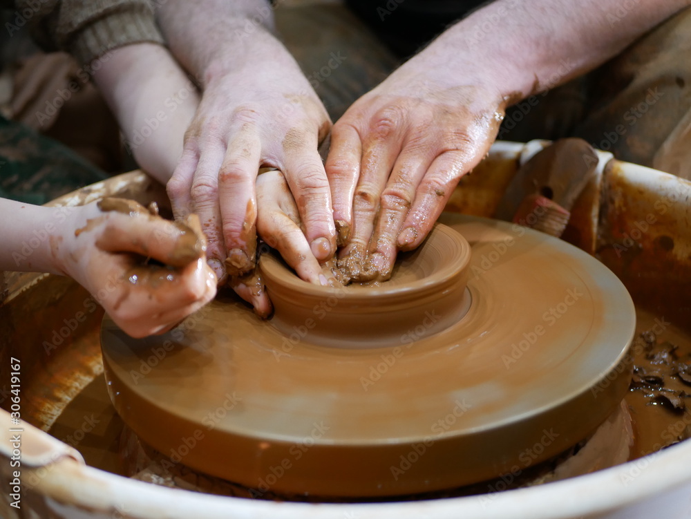 The master Potter teaches the child to make a clay jug on a modern Potter's wheel with an electric drive. The hands of a child and an adult man are stained with clay. Teaching pottery.