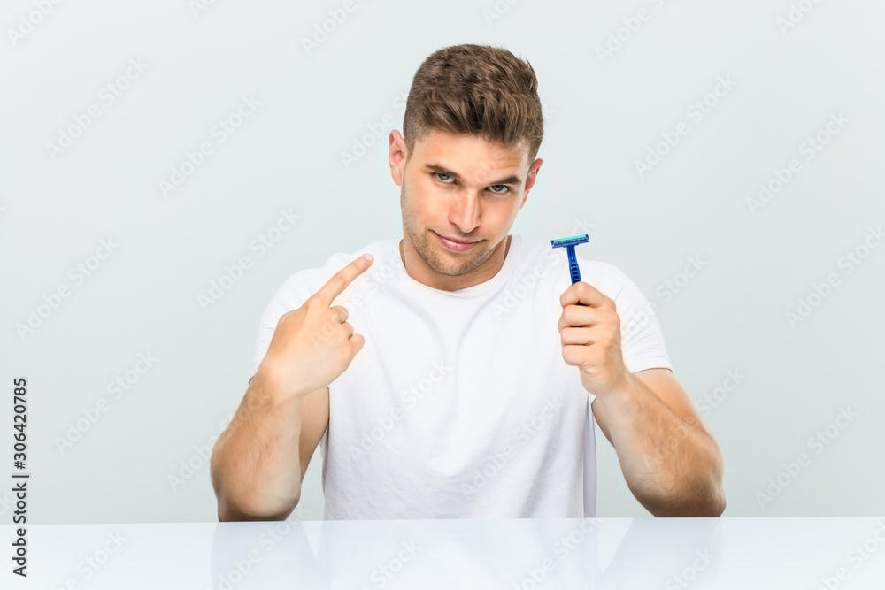 Young man holding a razor blade pointing with finger at you as if inviting come closer. Young man holding a razor blade pointing with finger at you as if inviting come closer.