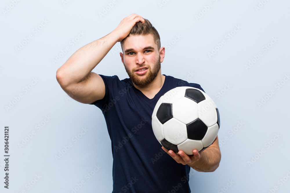 Young caucasian man holding a soccer ball being shocked, she has remembered important meeting.