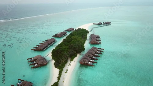 Aerial, reverse, drone shot, over a island, overlooking trees, bungalows and white sand beaches, in middle of the shallow, turquoise sea, on a cloudy day, on the Conrad Rangali island, in Maldives photo