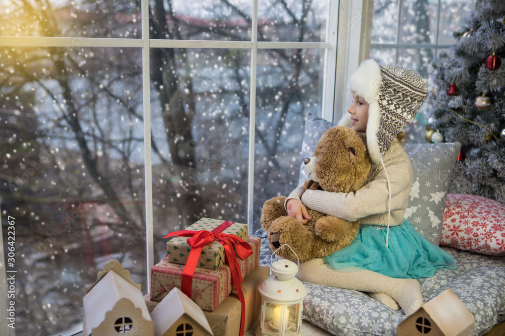 Fototapeta premium Little girl sitting by the window with a bear