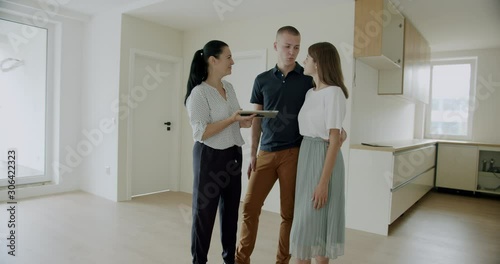 First time buyers electronically signing digital tablet in new house. Young couple buying their first home signing a contract on a digital tablet.