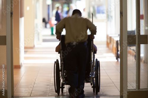 Rear view of man pushing patient on wheelchair at hospital corridor