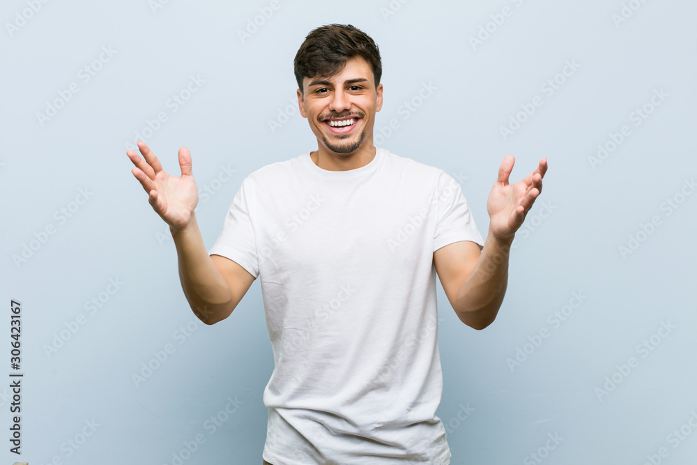 Young caucasian man wearing a white tshirt receiving a pleasant surprise, excited and raising hands. - obrazy, fototapety, plakaty 